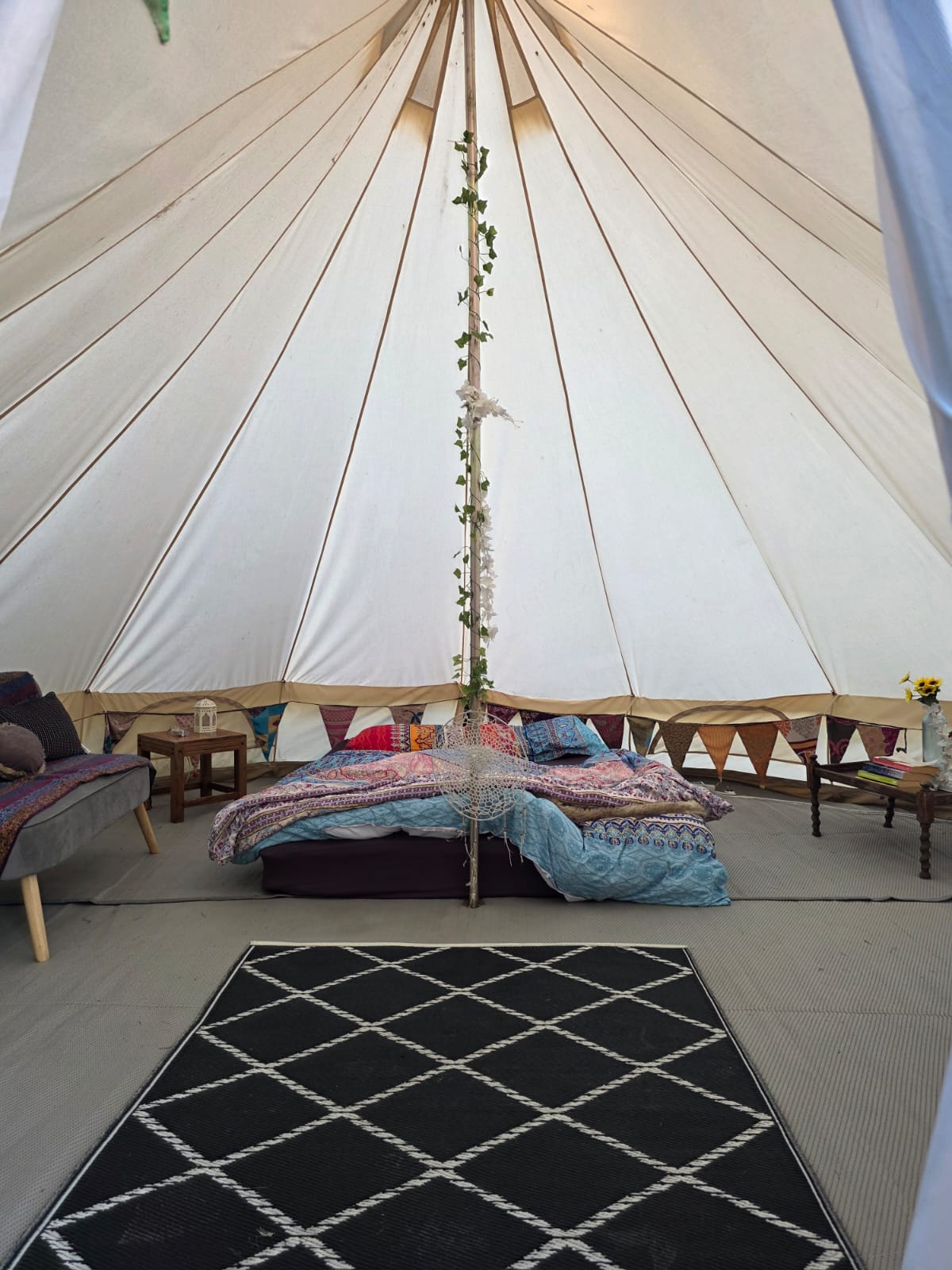 Inside a bell tent — double bed, bedding, rugs and lanterns